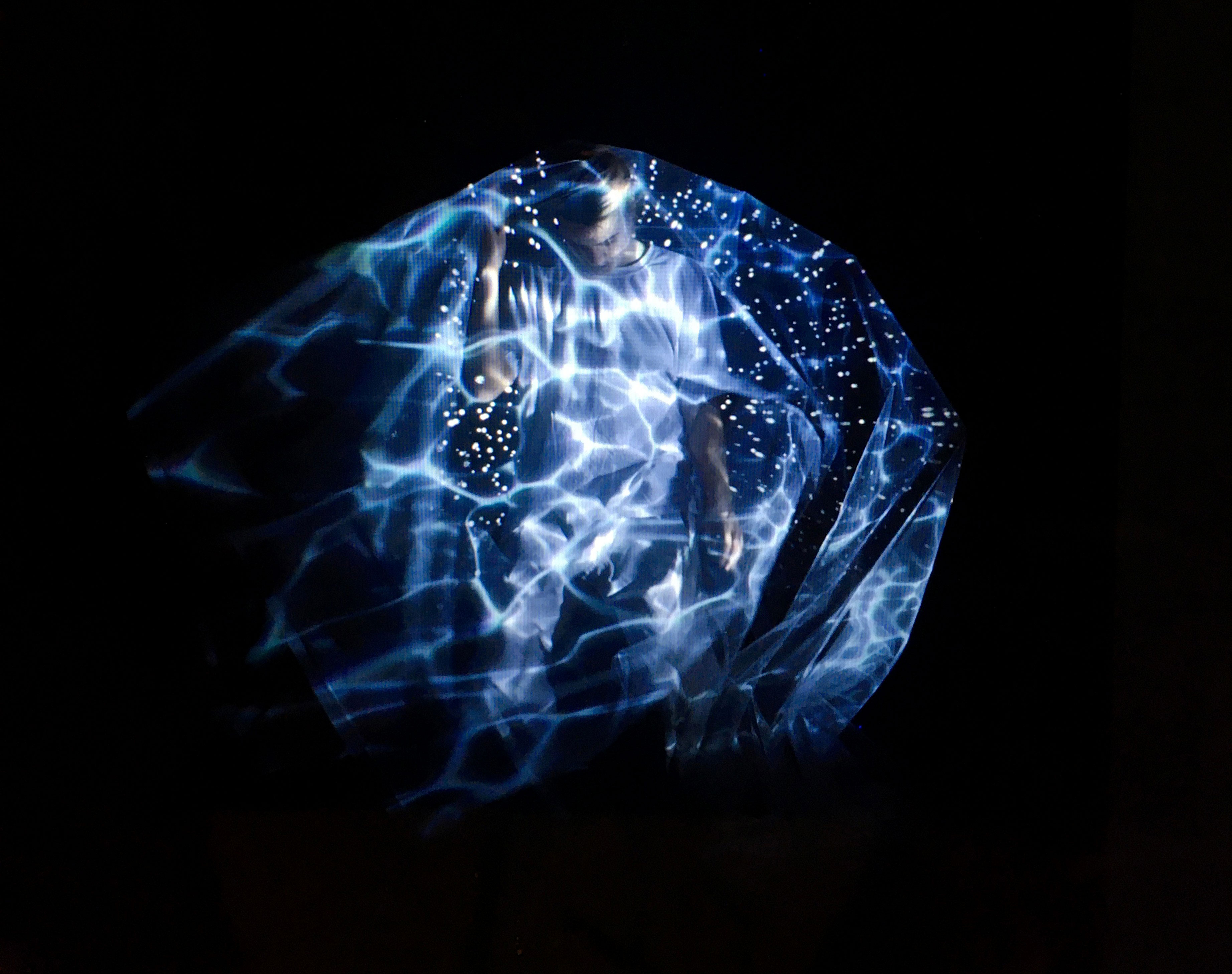 Blue water-caustic light wrapping a dancer against black